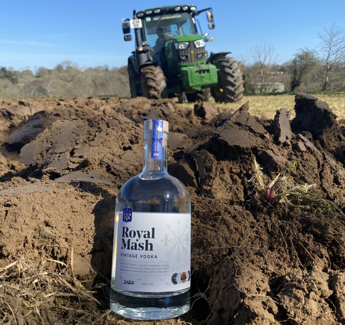 A bottle of Royal Mash Vintage Vodka in a field with a tractor behind it